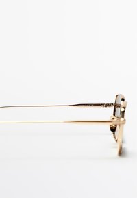 Zonnebril van metaal met goudkleurige afwerking en een dun montuur, met een rechthoekige vorm en slanke pootjes. Heldere glazen en subtiele merkdetails langs de armen.