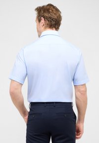 Lichtblauw korte mouwen shirt met een rechte snit, schone kraag en een gladde textuur, gecombineerd met donkere marineblauwe broek met achterzakken.