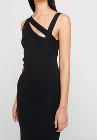 Abito nero aderente con scollatura asimmetrica e spalline larghe, caratterizzato da dettagli cut-out. Realizzato in materiale elastico per una vestibilità aderente.