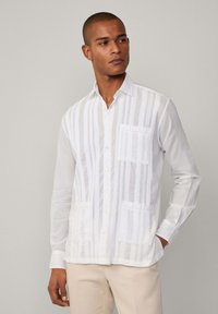 Biała koszula zapinana na guziki w pionowe paski, z dwiema przednimi kieszeniami. Wykonana z lekkiego materiału, z klasycznym kołnierzykiem i długimi rękawami.