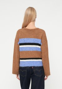 Rudas megztinis su horizontaliais mėlynos, juodos ir baltos spalvų dryžiais. Turi laisvą siluetą ir apvalų iškirpimą. Tekstūruota medžiaga.