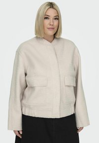 Helebeige lühike jakk tekstuurse kangaga, seisev krae ja kaks esist pockets. Varrukad on laiad ja disain on kastiline.