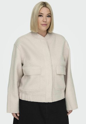 Lys beige cropped jakke med et tekstureret stof, stående krave og to forlommer. Ærmerne er brede, og designet er firkantet.