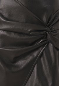 Sort læderstof med en glat tekstur, der fremhæver snoet detaljer og foldede lag. Designet understreger form og struktur.