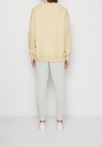 Ljusbeige bomullströja med sänkta axlar, kombinerad med ljusgrå mjukisbyxor och vita sneakers med rosa detaljer.