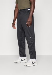 Black athletic pants with a sleek design, featuring a light gray Nike logo, side pockets, elastic waistband, and textured fabric.