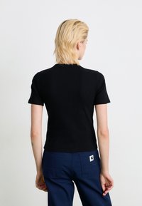 Sort kortærmet tætsiddende top med rund halsudskæring, lavet af ribbet stof; båret med navy blå bukser med baglommer.