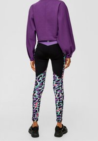 Sudadera corta púrpura con mangas voluminosas combinada con leggings negros que presentan un estampado animal multicolor y acentos texturizados.