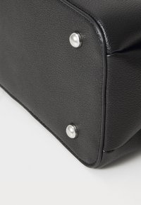 Coin de sac en cuir noir mettant en avant une surface texturée, des rivets en argent, et des détails de couture, soulignant sa forme structurée et sa durabilité.