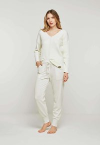 Weißer gerippter Strickpullover mit V-Ausschnitt und langen Ärmeln, kombiniert mit weißen, lässigen Jogginghosen mit seitlichen Taschen und elastischem Bund.