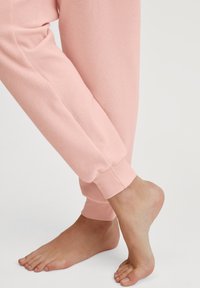 Roze joggingsbroek met een zachte textuur, voorzien van een elastische band bij de enkel en een gladde afwerking, gecombineerd met een blote voet.