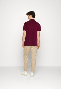 Polo shirt bordeaux avec un col classique, associé à un pantalon beige et des baskets blanches. Le tissu a une texture lisse.