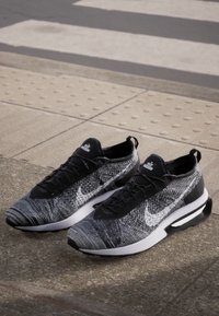 Baskets noires et blanches avec un upper en tricot texturé, mettant en avant un swoosh Nike proéminent, des lacets noirs et une semelle blanche rembourrée.