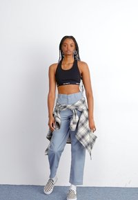 Black sports bra, light blue high-waisted pants, and a tied plaid shirt. Black and white checkered slip-on shoes, with long braided hair.