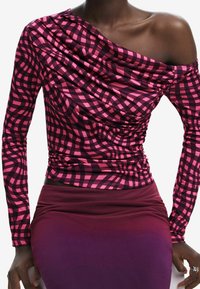 Pitkähiha, olkatonta toppia, jossa on roikkuva kaula-aukko, esittelee ruudullista kuosia vaaleanpunaisena ja mustana, yhdistettynä syvän burgundin väriseen hameeseen.