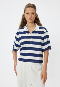 Tummansininen ja valkoinen raidallinen polo-paita, jossa on kaulus, lyhyet hihat ja rento istuvuus; mukana kaksi nappia ja näkyviä ompelutietoja.