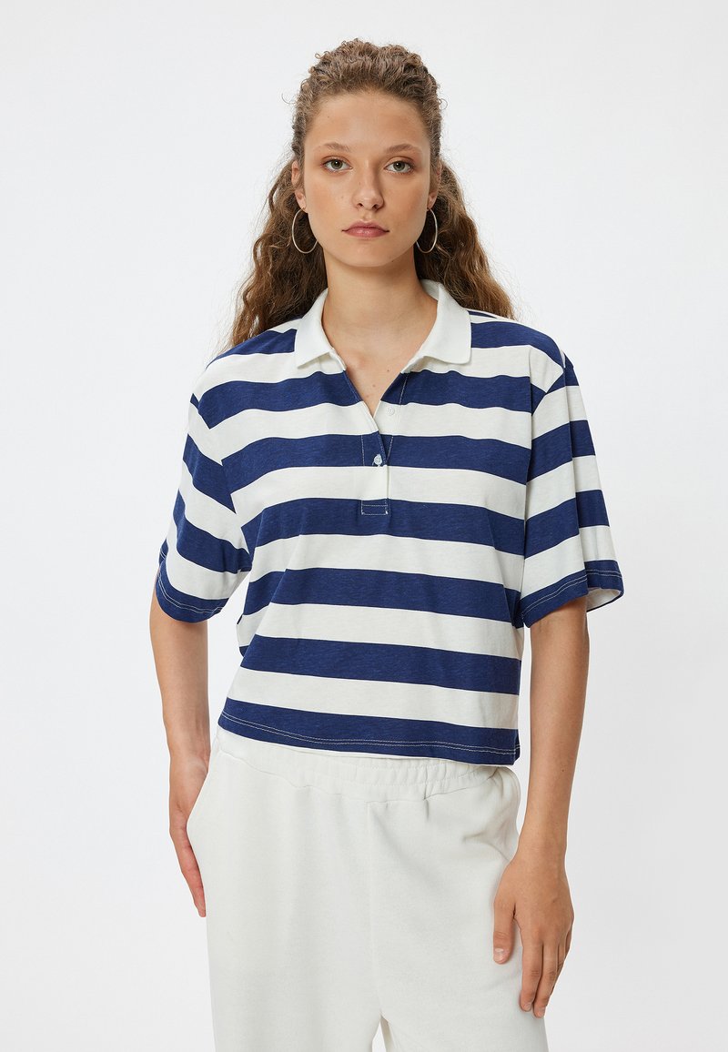 Tummansininen ja valkoinen raidallinen polo-paita, jossa on kaulus, lyhyet hihat ja rento istuvuus; mukana kaksi nappia ja näkyviä ompelutietoja.