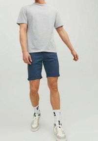 Szaro-biała, w paski, koszulka z krótkim rękawem w połączeniu z granatowymi spodniami typu bermudy. Białe sneakersy z szarymi akcentami oraz wzorzyste skarpetki.