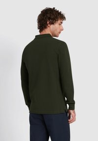 Donkergroen langslievend shirt van textuurstof. Beschikt over een kraag en zijsplitten aan de onderkant, met knoopsluiting bij de mouwen.