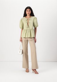 Blusa verde chiaro con maniche a sbuffo, scollo a chiave e vita a peplum. Abbinata a pantaloni beige a gamba larga e una borsa bianca.