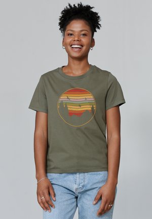 Olive green cotton t-shirt featuring a circular graphic with a sunset and silhouettes of trees in orange, pink, and yellow tones.