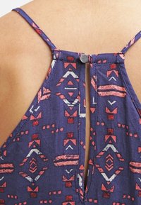 Haut à bretelles à motif marine avec des motifs géométriques en rouge et blanc, doté de bretelles ajustables et d'une fermeture à bouton au dos.