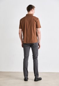 Barna, rövid ujjú galléros póló, szürke, slim-fit nadrággal és fekete slip-on cipővel párosítva. Egyszerű, letisztult dizájn.