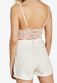 Růžový krajkový bralette s nastavitelnými ramínky, spárovaný s bílými kraťasy se zahnutým lemem, které mají zadní kapsy a strukturovanou tkaninu.