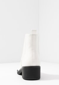 Bottines blanches à texture crocodile, tige lisse et petit talon bloc noir. Dotées d'une languette à l'arrière pour un enfilage facile.