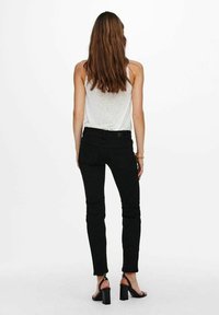 Svarta denimjeans med en tajt design, medelhög midja och ankellång skärning. Bärs med en ljusgrå linne och svarta klacksandaler.