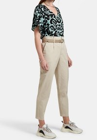 Blusa nera con motivo verde menta, pantaloni beige a vita alta, cintura beige con borchie e sneakers voluminosi. Tessuto morbido, vestibilità rilassata.