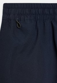 Cintura elástica azul marino con costura fruncida y un pequeño detalle de lazo de rayas en blanco y negro.