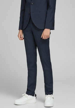 Pantalones de traje azul marino confeccionados en tejido texturizado, combinados con zapatillas blancas. Diseño ajustado con pierna cónica y detalles sutiles en los bolsillos.