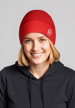 Bonnet en tricot rouge à texture lisse avec un logo blanc sur le côté, porté avec un sweat à capuche noir.