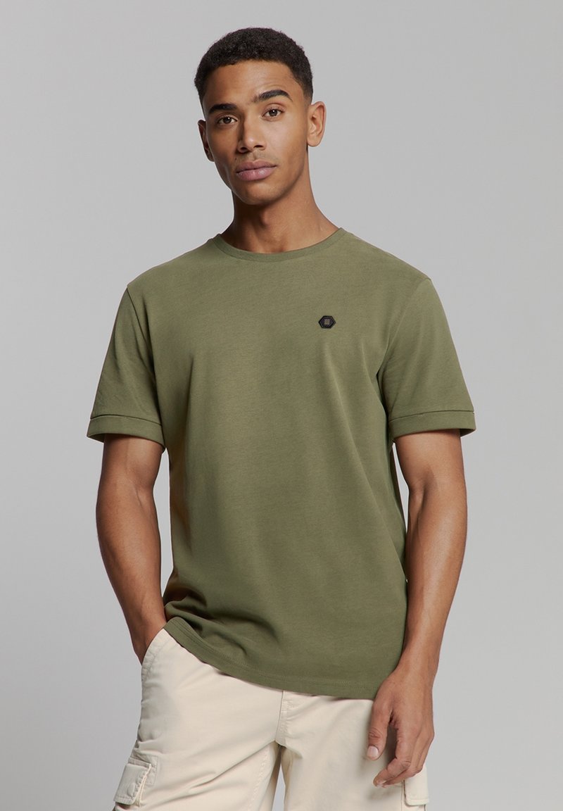 Olijf groene katoenen T-shirt met ronde hals en korte opgerolde mouwen. Heeft een klein zwart zeshoekig merklogo op de borst.