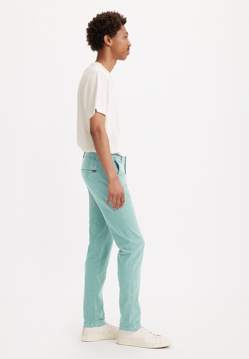 Pantalones de denim azul claro con corte recto, combinados con una camisa blanca de manga corta y zapatillas blancas, mostrados de perfil.