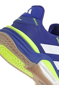 Blauwe sportieve schoen met een gestructureerde mesh bovenzijde, witte accenten, een neongroene zool en een geribbelde rubberen buitenzool voor grip.