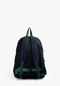 Mochila azul marino con detalles verdes, que cuenta con correas acolchadas, panel trasero de malla y hebilla ajustable. Textura suave, diseño aerodinámico.