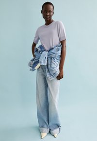 Lichtpaarse短-sleeve shirt gecombineerd met lichtblauwe wijde jeans. Spijkerjack om de taille geknoopt, met klassieke zakken en stiksels.