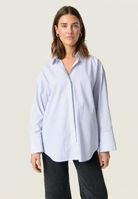 Striped button-up shirt in light blue and white, featuring a relaxed fit, pointed collar, and wide cuffed sleeves.