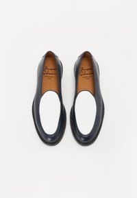 Leather loafers featuring a navy exterior, white elastic panel, and rounded toe. Contrasting black sole with subtle texture details.