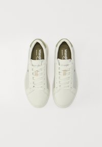 Sneakers bianche con un upper sintetico liscio, un accento sul tallone verde a contrasto e lacci piatti. Logo "Wrangler" visibile sulla linguetta.