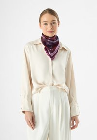 Seidenschal in sattem Burgund mit floralen und textrischen Mustern, kombiniert mit einer cremefarbenen Bluse. Der Schal hat einen kontrastierenden lila Rand.