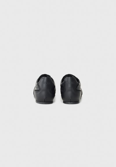 Black leather sneakers with a smooth texture, featuring curved side accents and branding on the heel. Low profile design with a rounded toe.