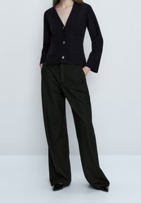 Navy cardigan with v-neck, two front pockets, and gold buttons, paired with high-waisted black wide-leg trousers and pointed black heels.