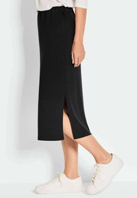 Schwarzer, knöchellanger Rock aus glattem Stoff mit einem seitlichen Schlitz. Kombiniert mit weißen Sneakers, die einen lässigen Bund und ein einfaches Design aufweisen.