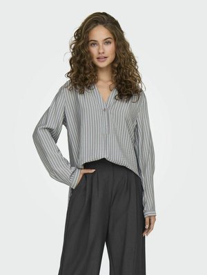 Gestreepte button-up shirt in grijs en wit, gecombineerd met hoge donkere wijde broek; losse fit met lange mouwen en manchetten.