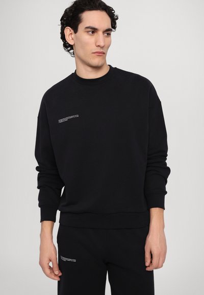 Schwarzer Pullover aus weicher Stoffqualität mit Rundhalsausschnitt. Mit kleinem weißen Text auf der Brust. Lange Ärmel mit gerippten Bündchen und Saum.