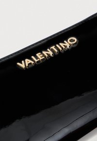 Carteira de pele vernizada preta com o logótipo "VALENTINO" em relevo dourado na frente, apresentando um acabamento suave e brilhante.