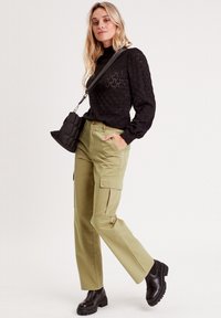 Pull noir texturé avec des manches longues, un pantalon cargo vert olive et des bottines noires à semelles épaisses, associé à un petit sac à bandoulière noir.